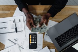 7 Ways To Finance Your MBA - iphone calculator app, woman counting dollars with a laptop by her side.